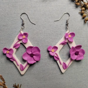 Handmade diamond-shaped polymer clay earrings with small purple flowers and purple leaves, displayed on a neutral background.