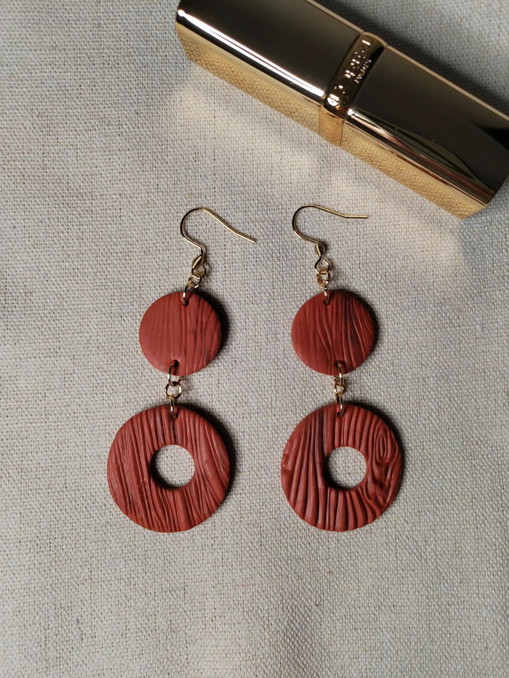 Handgemachte Ohrringe aus Polymer Clay in Terrakotta mit Holzstruktur, bestehend aus zwei runden Elementen, flach auf Leinentuch fotografiert,