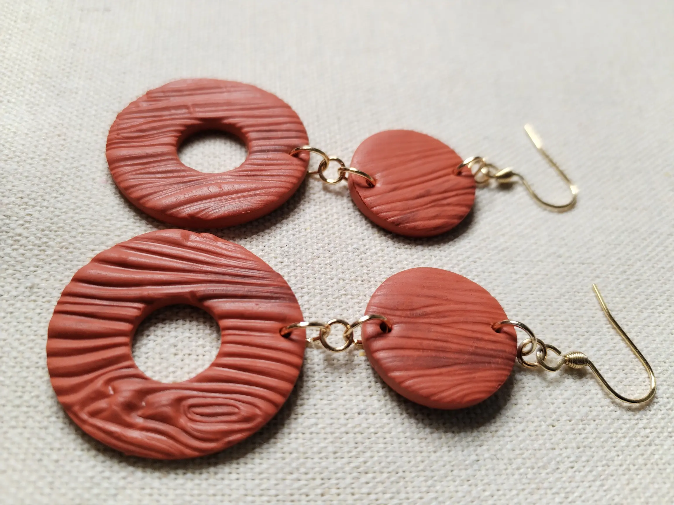 Handgemachte Ohrringe aus Polymer Clay in Terrakotta mit Holzstruktur, bestehend aus zwei runden Elementen, flach auf Leinentuch fotografiert,