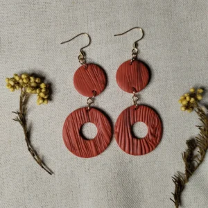 Handgemachte Ohrringe aus Polymer Clay in Terrakotta mit Holzstruktur, bestehend aus zwei runden Elementen, flach auf Leinentuch fotografiert, mit Trockenblumen dekoriert