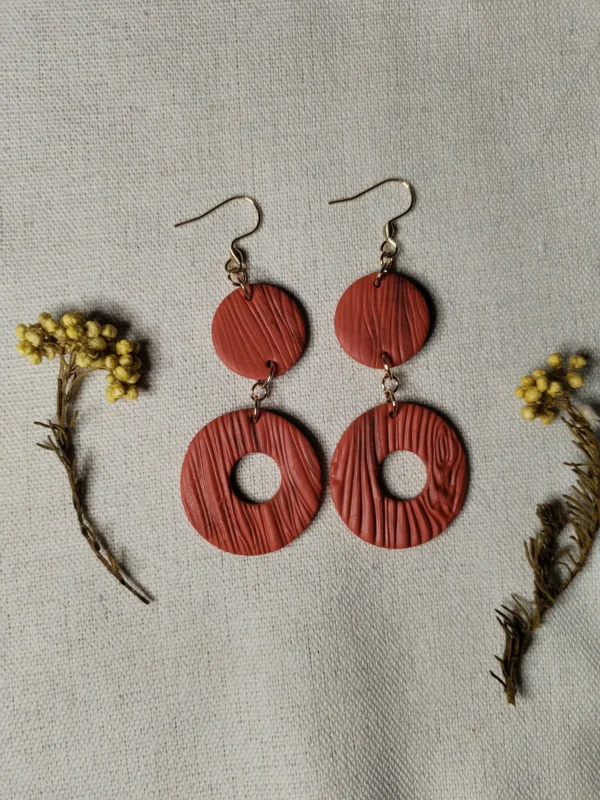 Handgemachte Ohrringe aus Polymer Clay in Terrakotta mit Holzstruktur, bestehend aus zwei runden Elementen, flach auf Leinentuch fotografiert, mit Trockenblumen dekoriert