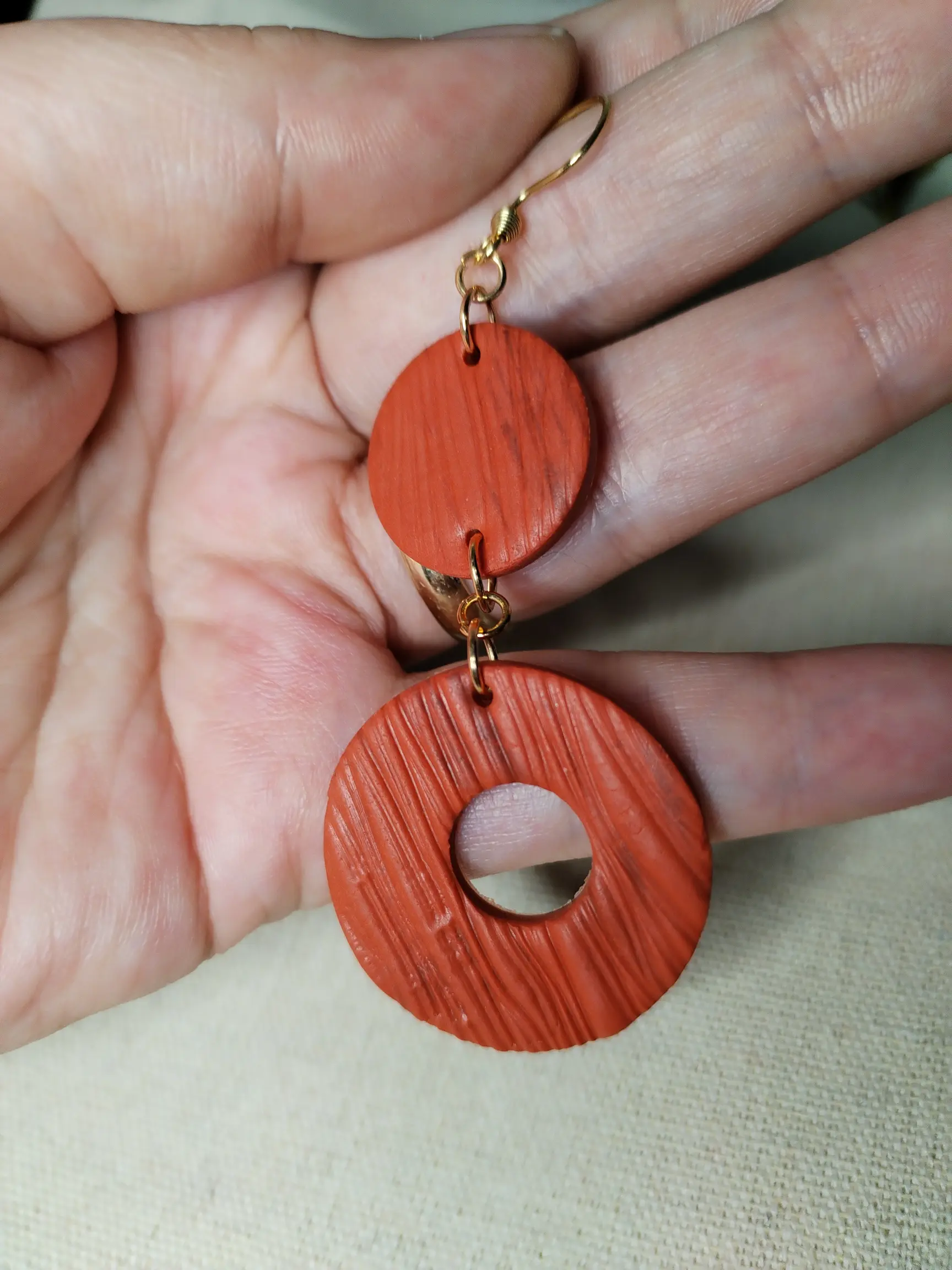 Handgemachte Ohrringe aus Polymer Clay in Terrakotta mit Holzstruktur, bestehend aus zwei runden Elementen, flach auf Leinentuch fotografiert.